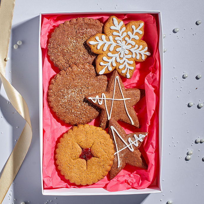 Box of assorted cookies including a snowflake and star-shaped gingerbread cookie on pink tissue paper.
